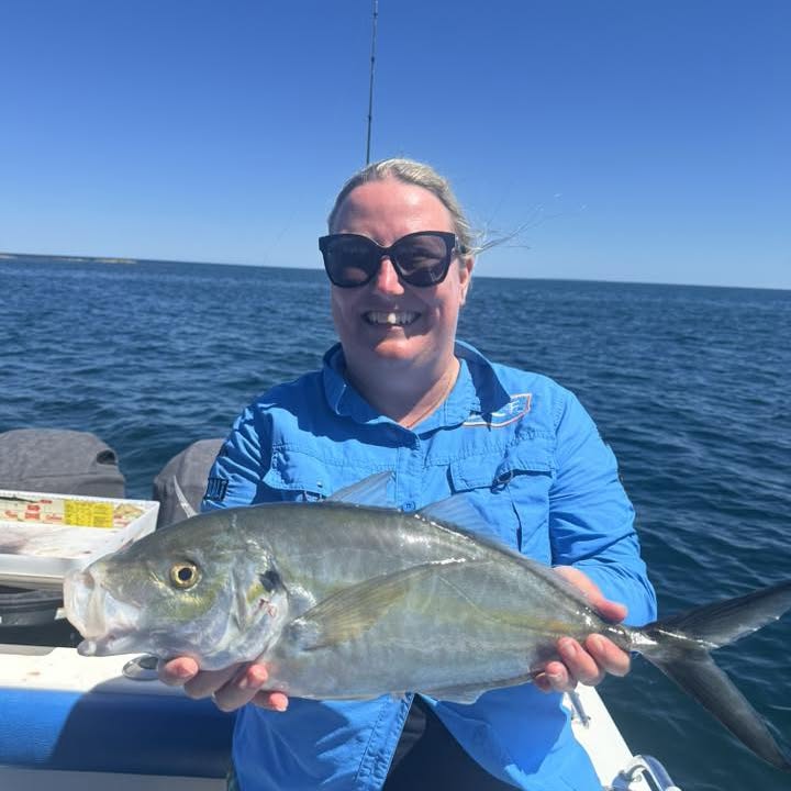 A guest holding a trevally with the coastline behind