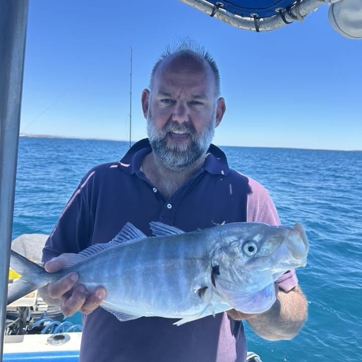 An angler holding a trevally on deck