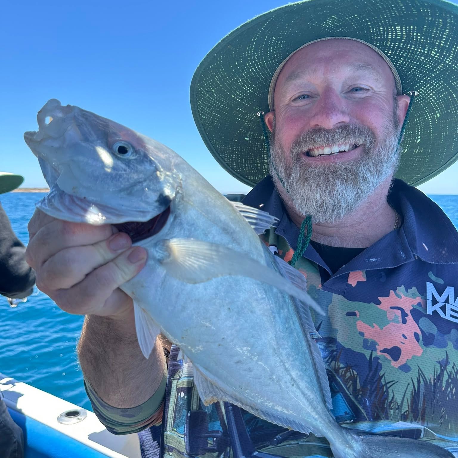 A smiling angler in a wide brimmed hat holding up a big trevally